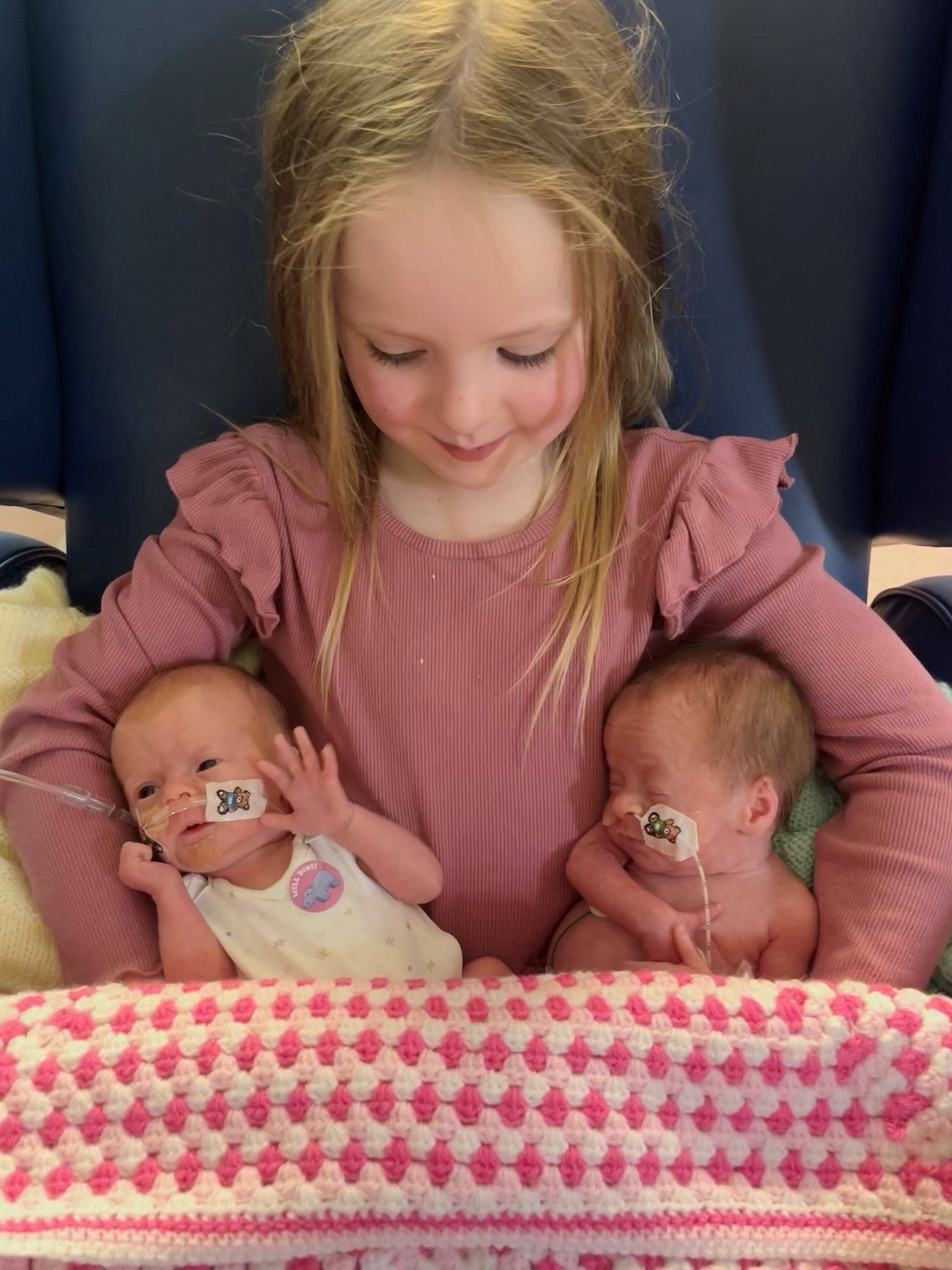 Two of three triplets being held by their older sister.